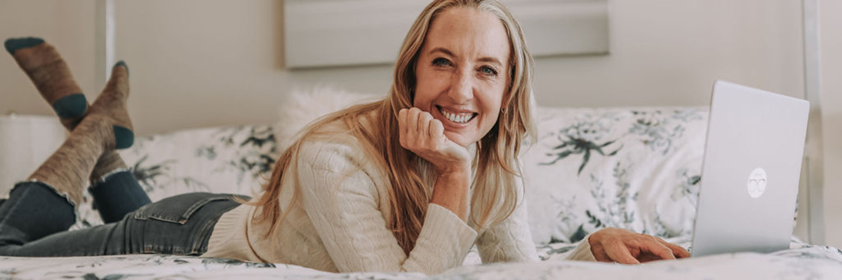Meg Urie Rab of A Mindful Midlife lays on a bed with her laptop